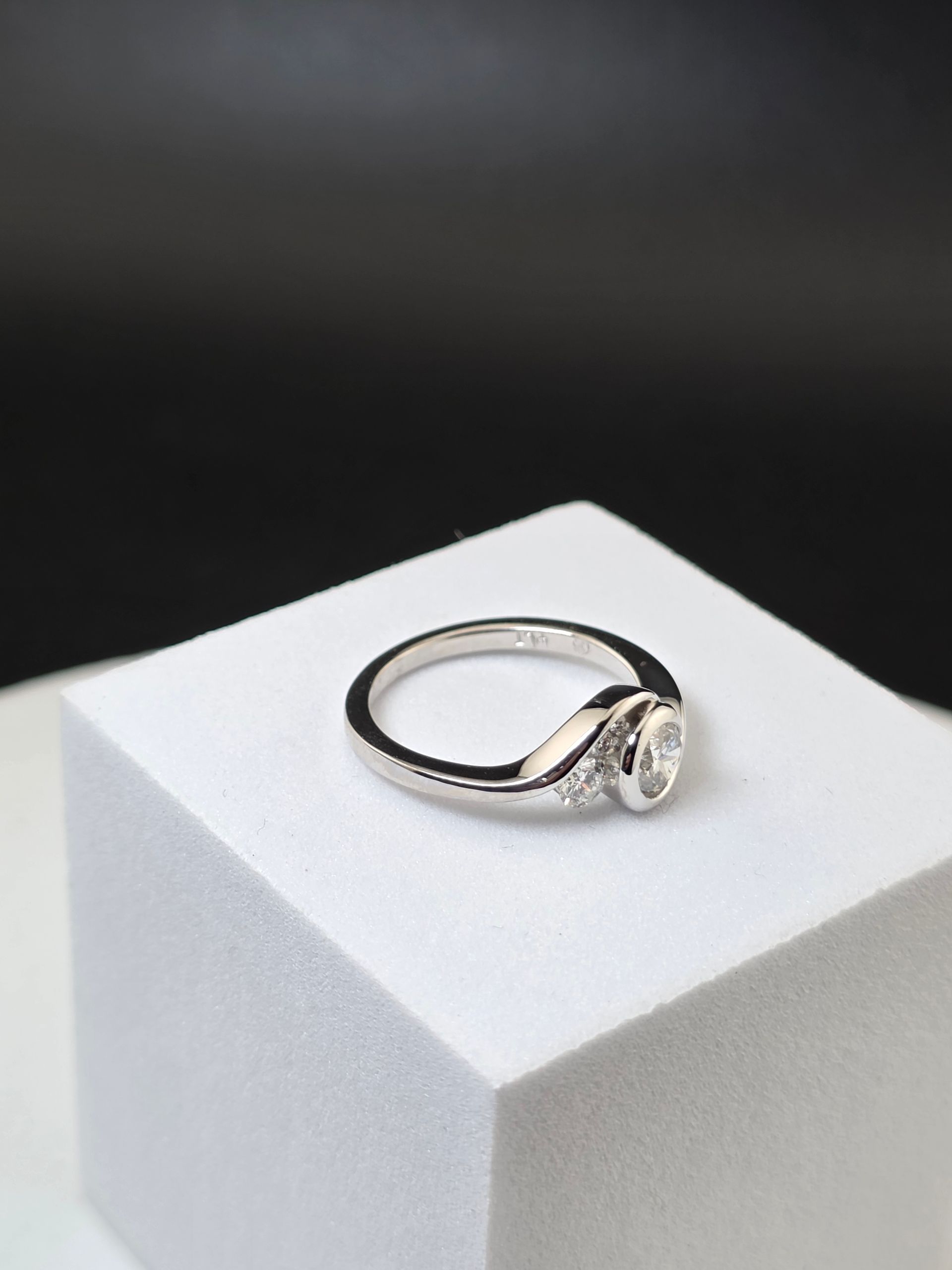 Silver ring with a diamonds on a white pedestal against a dark background