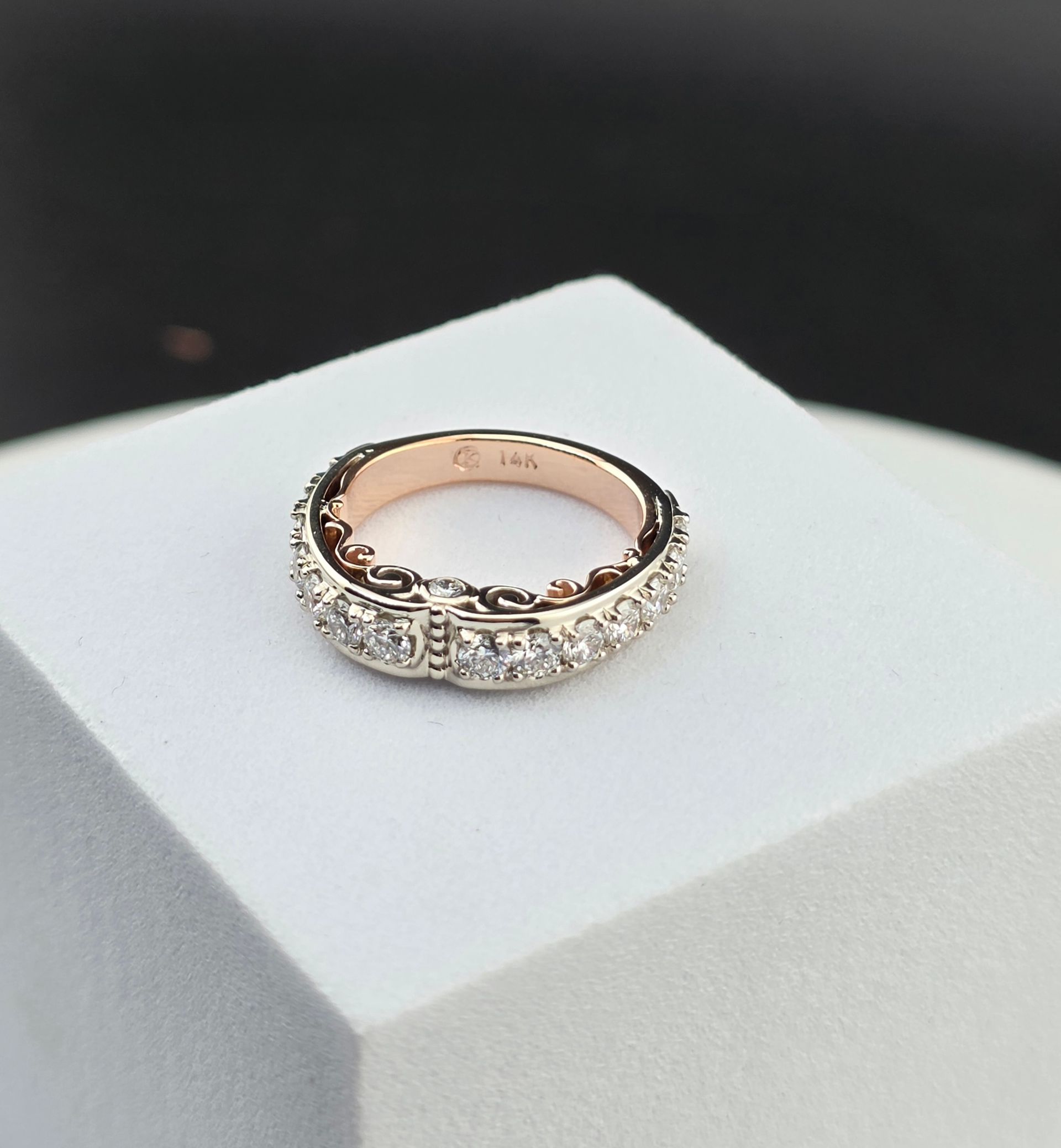 Rose gold diamond ring on a white display stand against a dark background