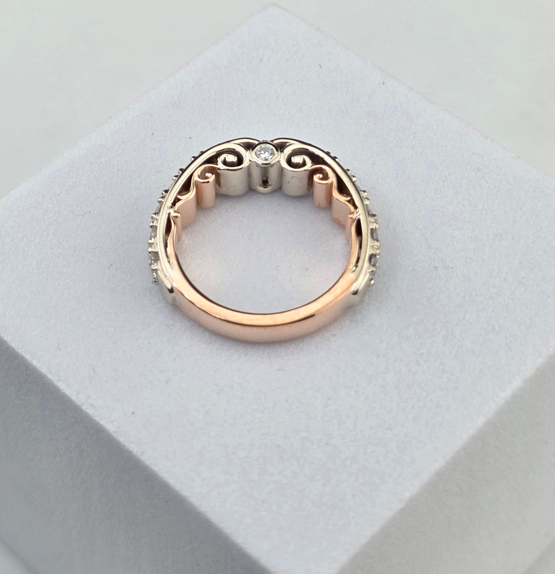 Rose gold ring with small diamond accents on a light gray display pedestal