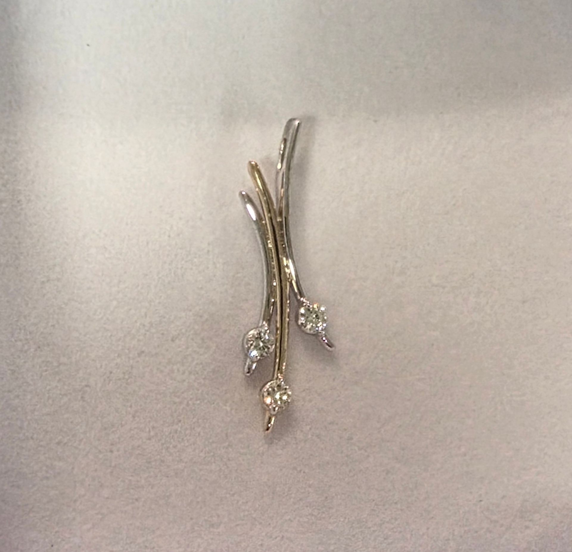Silver and gold leaf-shaped pendant with small white diamonds on a beige background