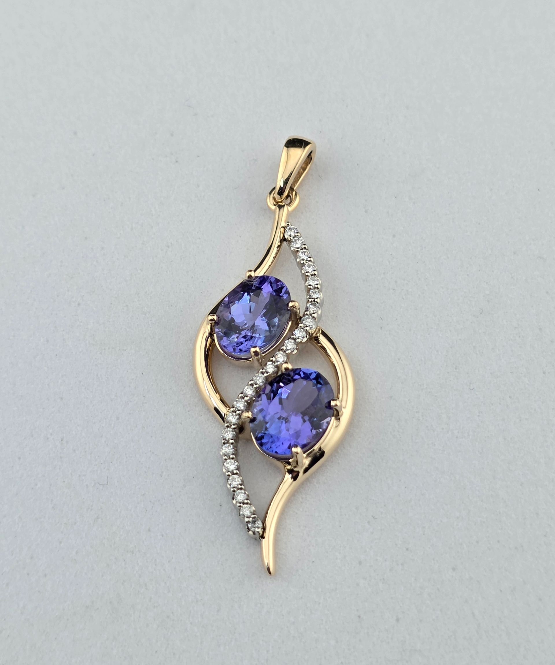 Gold pendant with two blue tanzanite gemstones and a curved line of small diamonds.