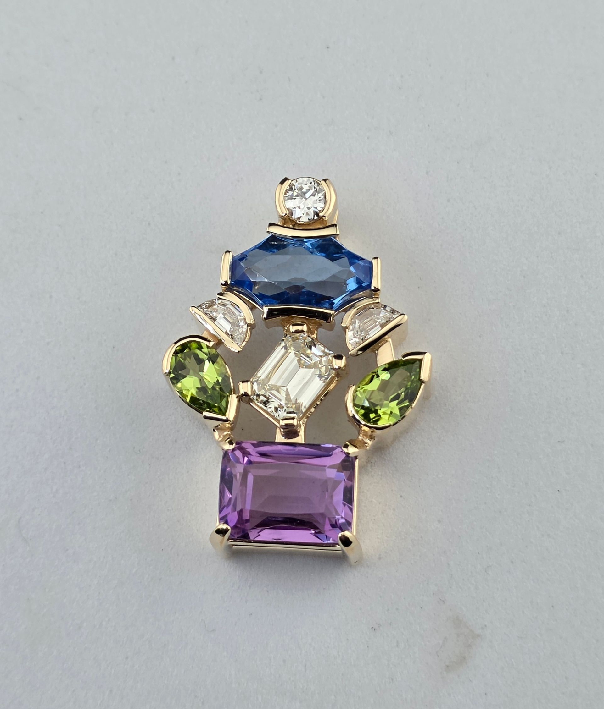 Gold jewelry slide pendnant with blue, green, clear, and purple gemstones on a gray background
