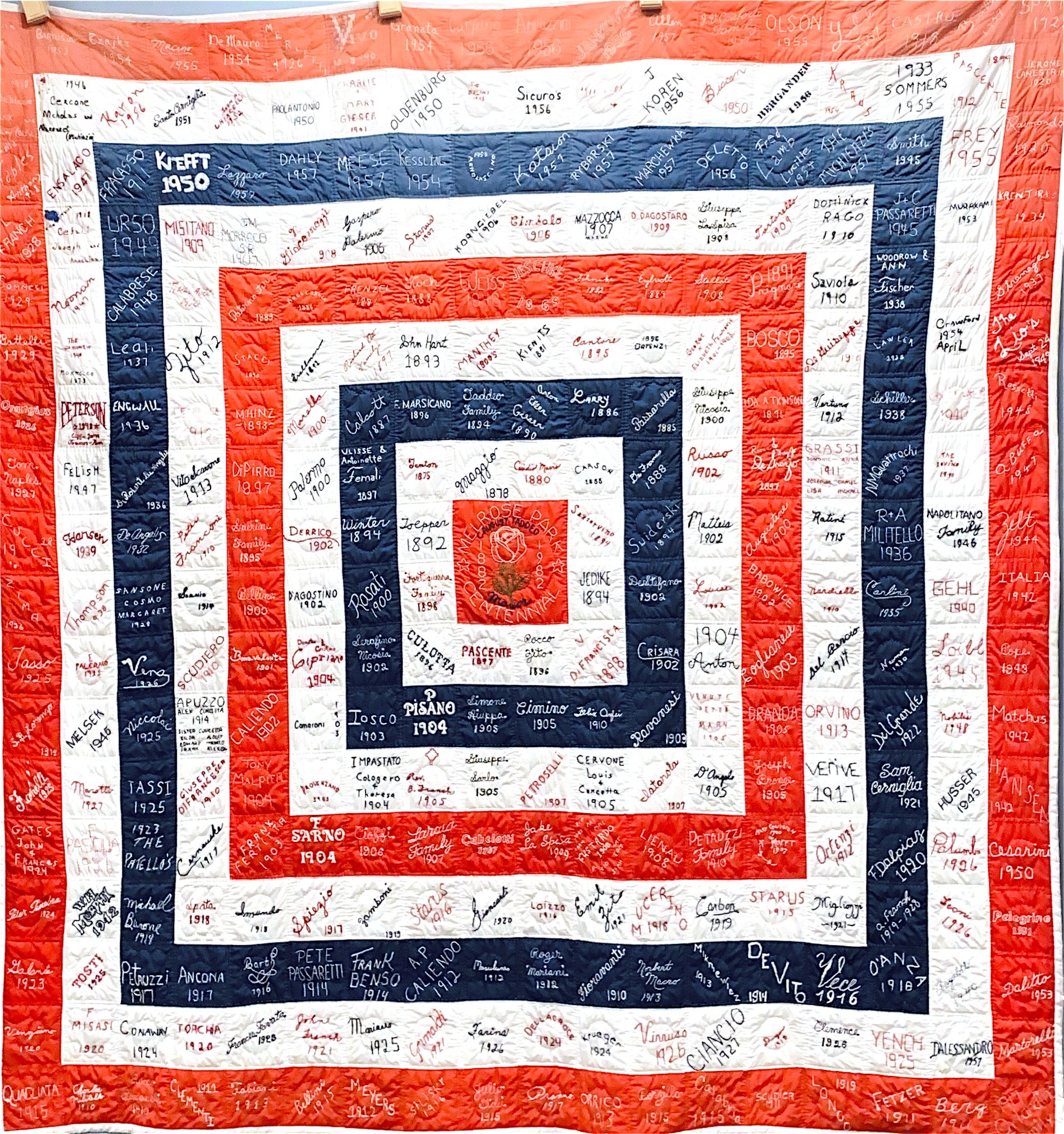 A red, white, and blue quilt featuring a pattern of concentric square frames, each covered in signatures and dates.