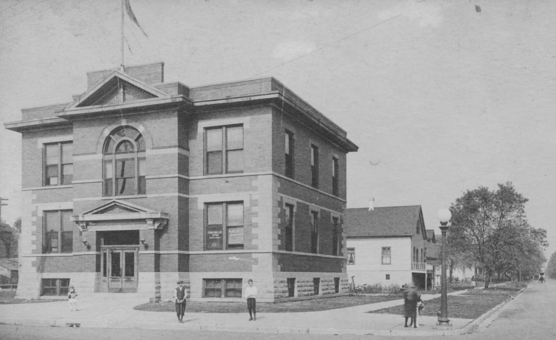 The entrance to the North Platte Public Library, featuring a green awning, brick exterior, metal ramp, and a green bench.