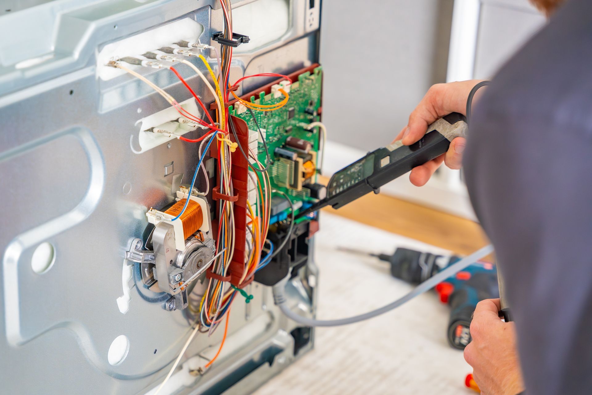 Technician testing exposed wiring inside a metal appliance with a multimeter