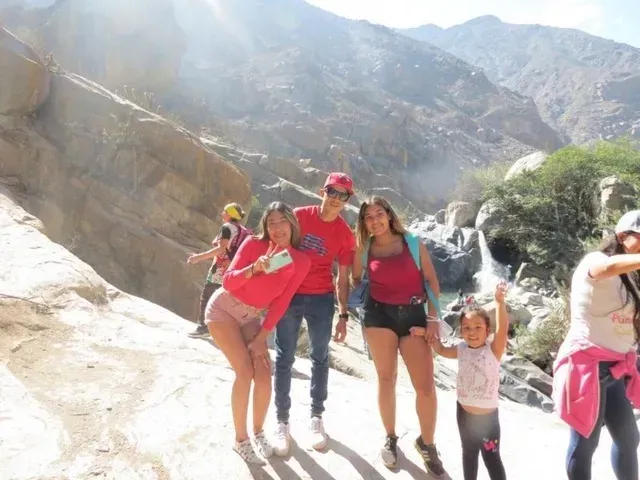 Un grupo posando en un sendero rocoso de montaña junto a una cascada, vestidos con ropa roja y rosa.