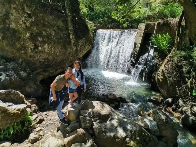 Tres personas posando sobre unas rocas junto a una pequeña cascada en un arroyo forestal.