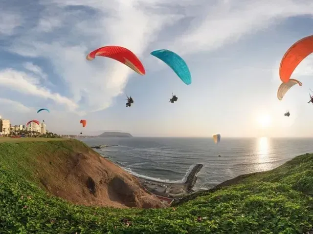 Al atardecer, unos parapentistas sobrevuelan un acantilado costero, con las olas del océano