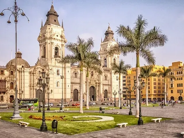 Catedral histórica y edificios coloniales amarillos junto a una plaza verde con palmeras y farolas.