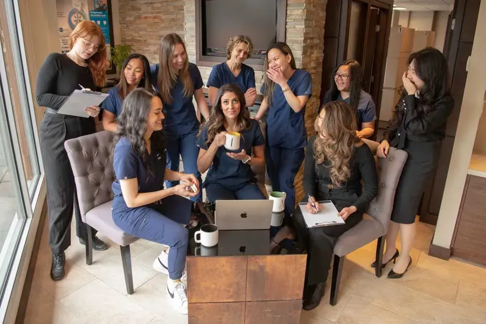 Group of women in office, some wearing scrubs, laughing, around a table with a laptop.