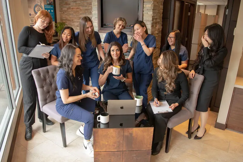 Medical team in blue scrubs and business attire, gathered around a coffee table, smiling, working.