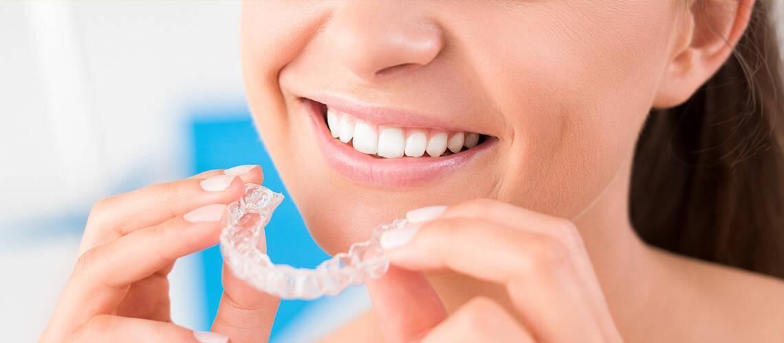 Woman smiling while holding a clear dental aligner near her mouth