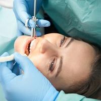 Dentist using blue gloves and a dental drill on a patient in a clinic chair