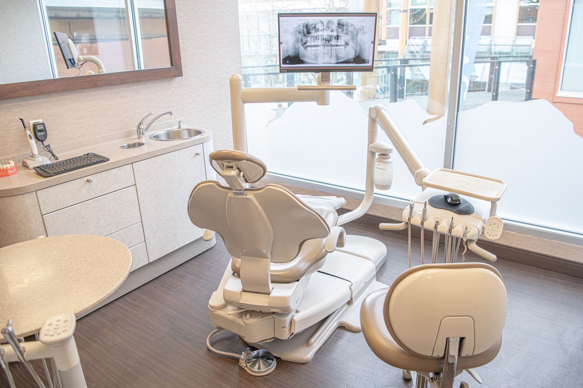 Bright dental exam room with chair, sink, cabinets, and large windows