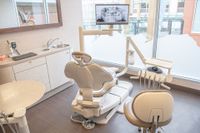 Bright dental exam room with chair, sink, cabinets, and large windows