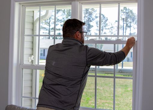 Man opening a white-framed window with a grid pattern. Exterior view: green lawn, houses, and a lamppost.