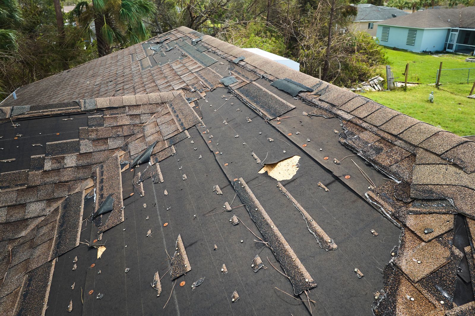 Damaged shingle roof with missing sections and exposed underlayment near the ridge.