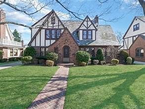 Tudor-style brick house with a peaked roof, green lawn, and a stone walkway under a blue sky.