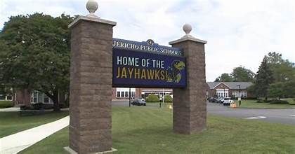 School entrance sign reading “Home of the Jayhawks” between two brick pillars