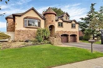 Large beige suburban house with stone accents, arched garage, and a manicured green lawn under a blue sky
