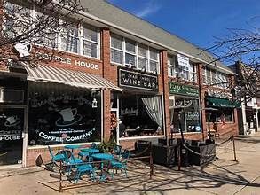 Outdoor brick storefronts with a coffee shop and wine bar, plus blue patio tables on a sunny street.