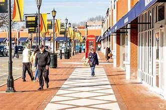 Pedestrian shopping street with people walking beside storefronts and lampposts on a sunny day