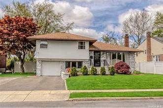 Suburban two-story house with a white exterior, red roof, green lawn, and driveway