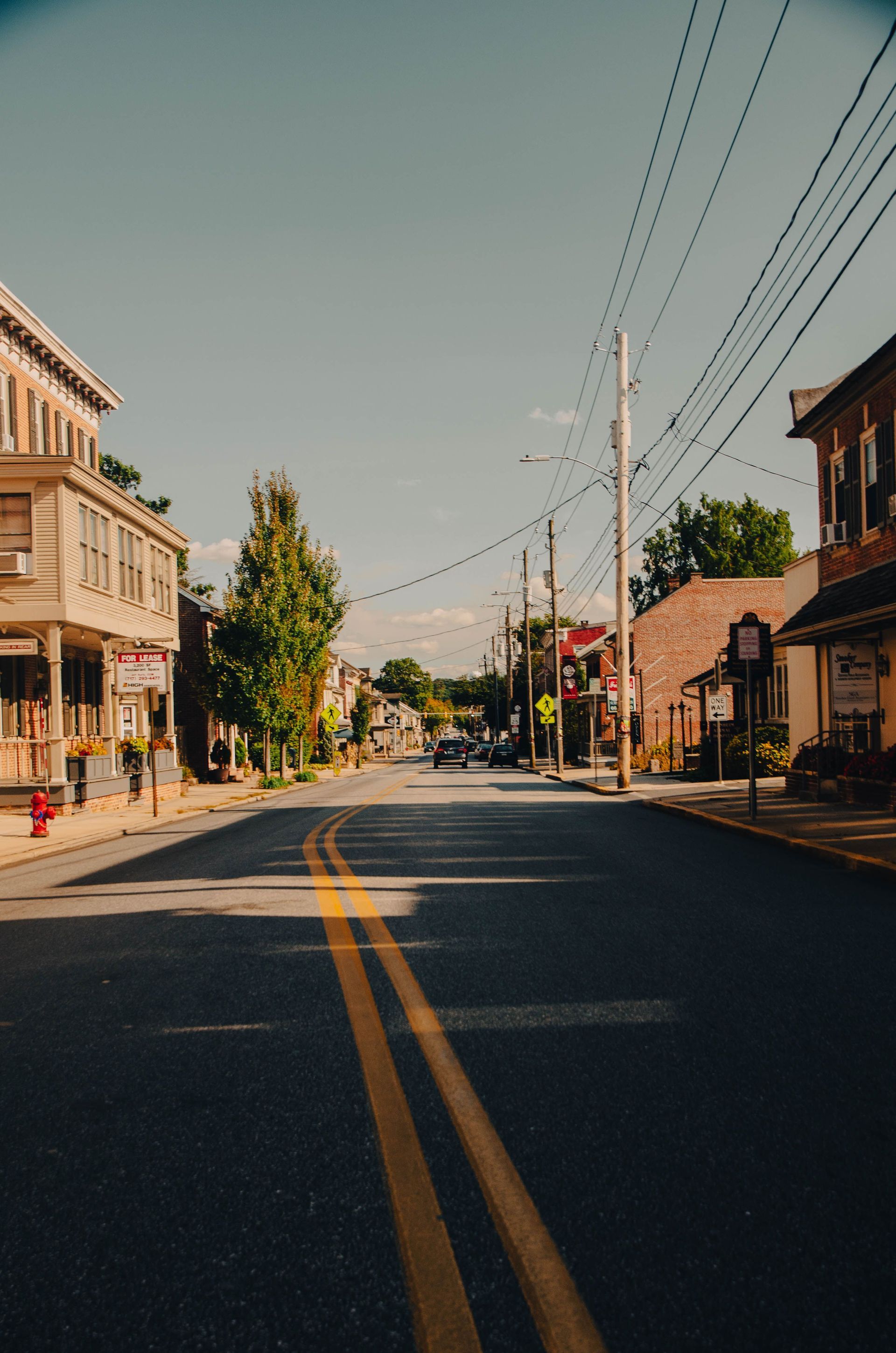 Empty small-town street with double yellow lines, buildings, and overhead power lines in bright sunlight
