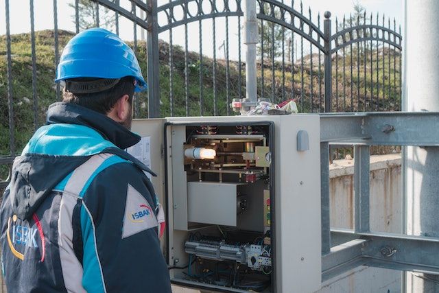 Electrician in a blue hard hat inspecting a fuse box
