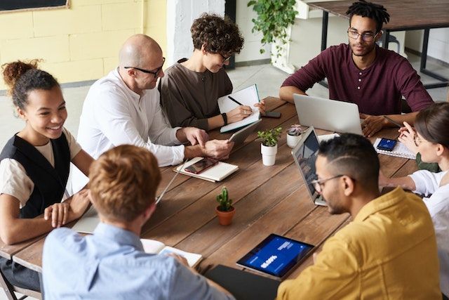 People sitting at wooden table with laptops and notebooks
