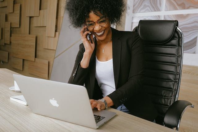 Person taking a phone call at their desk, with their laptop open