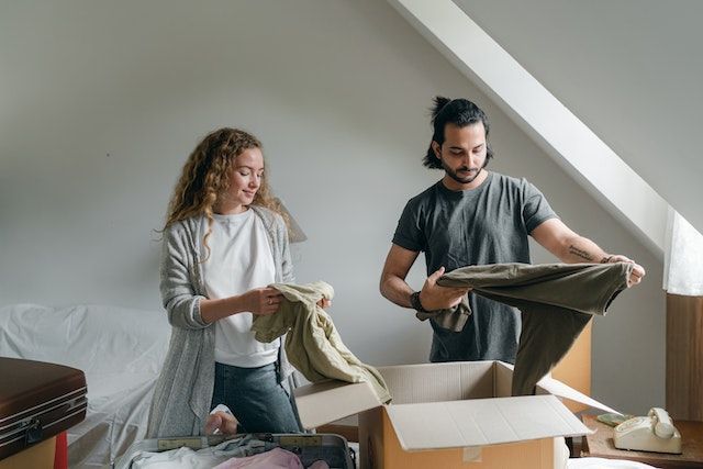 A couple unpacking clothes from brown cardboard boxes