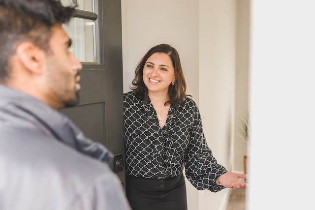 Person holding a door open and welcoming someone into a property