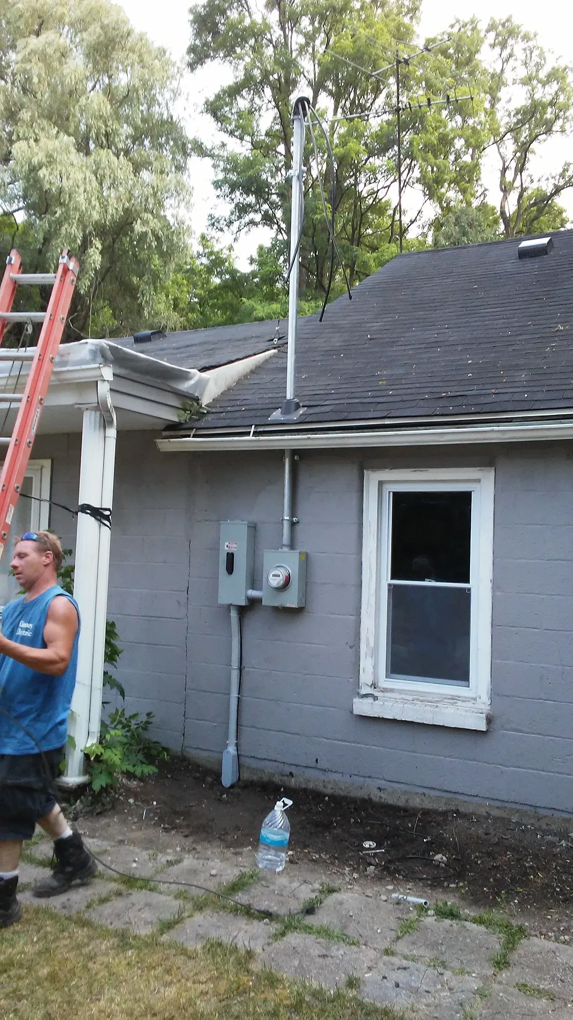 Gray house exterior with ladder, utility meters, and a man standing near the side yard