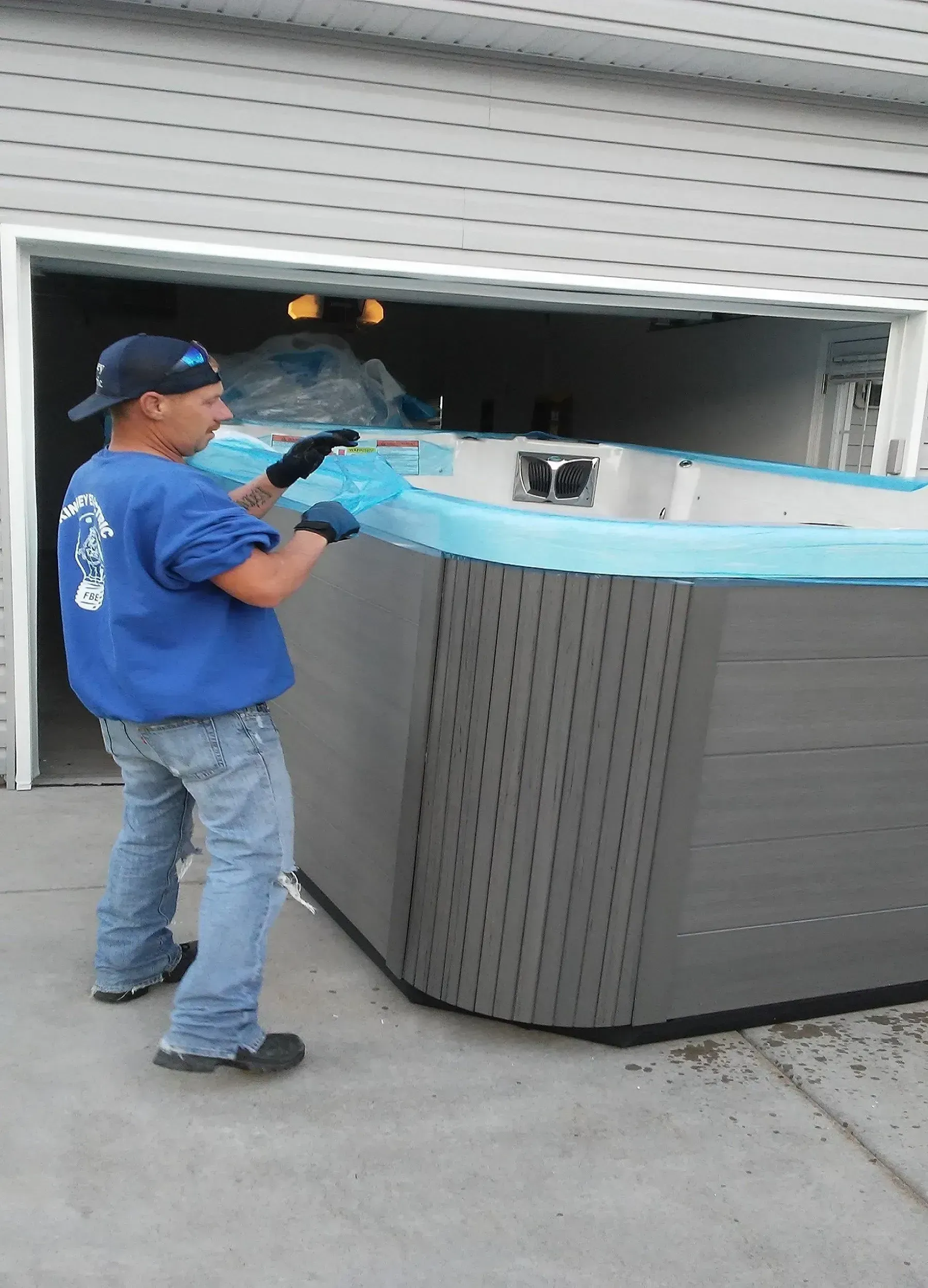 Worker in blue uniform moving a long metal panel beside a gray dumpster