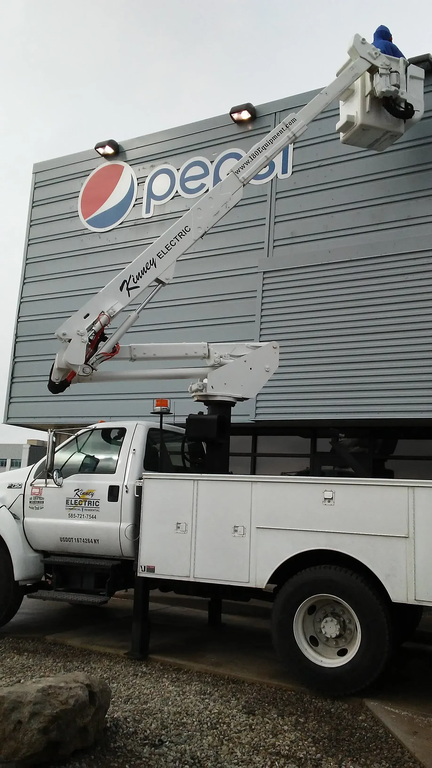 Utility truck with raised bucket lift beside a building facade with the Pepsi logo.