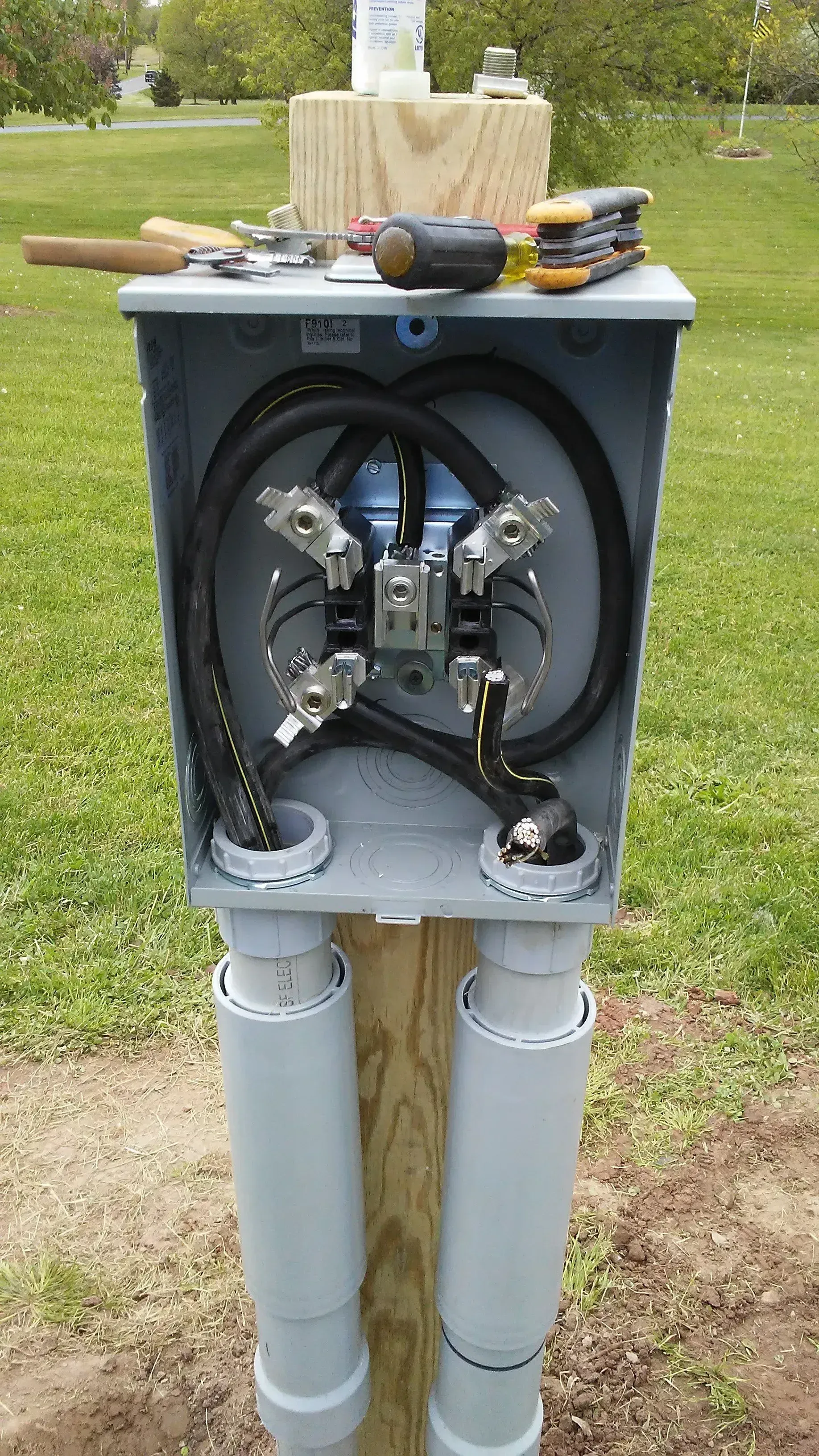 Open electrical utility box with exposed wiring mounted on two gray pipes outdoors.