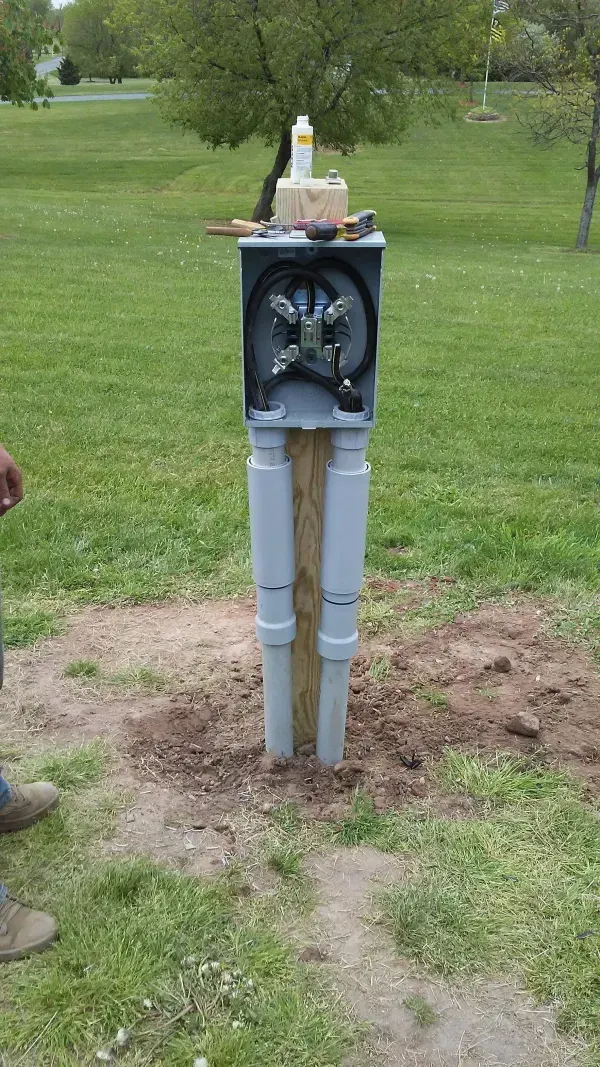Gray electrical meter pedestal in a grassy yard, with a small device mounted on top.