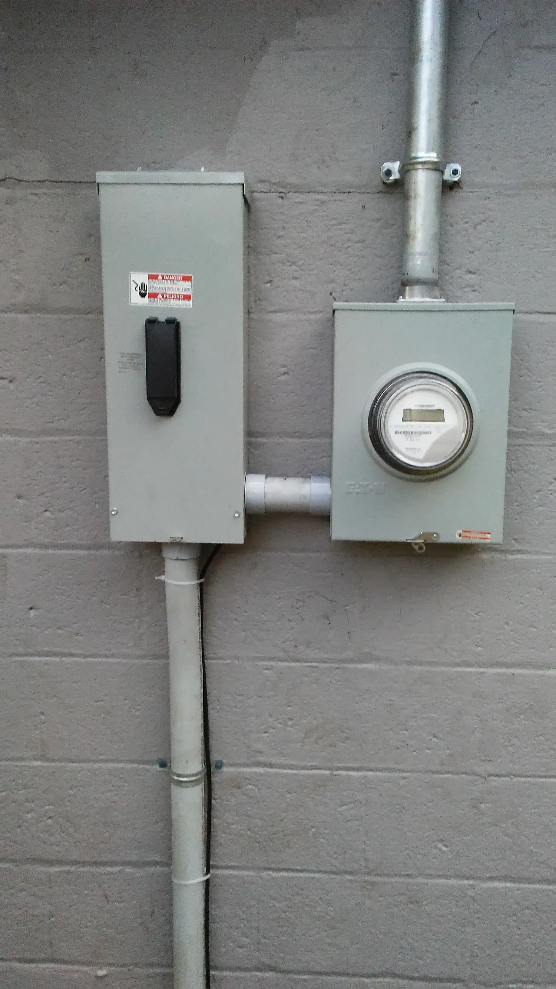 Gray electrical meter boxes mounted on a cinderblock wall with conduit piping
