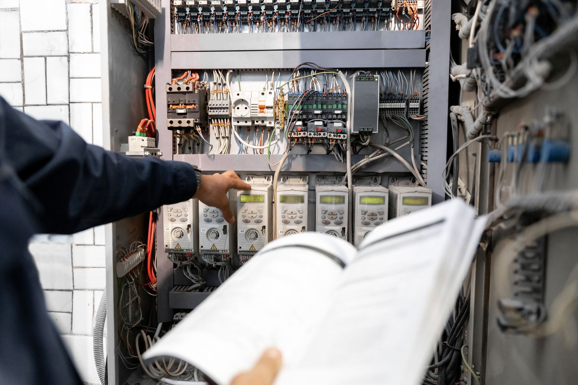 Technician pointing inside an open electrical control panel with wires and circuit components