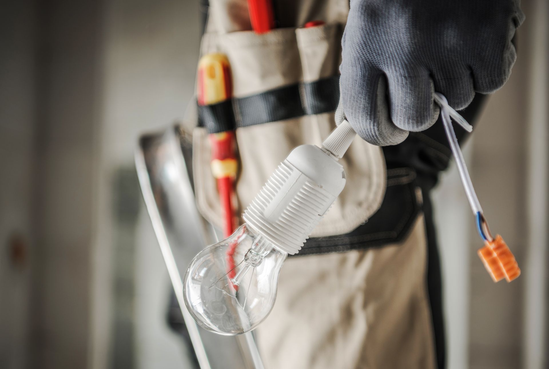 Gloved electrician holding a light bulb and wires during installation work