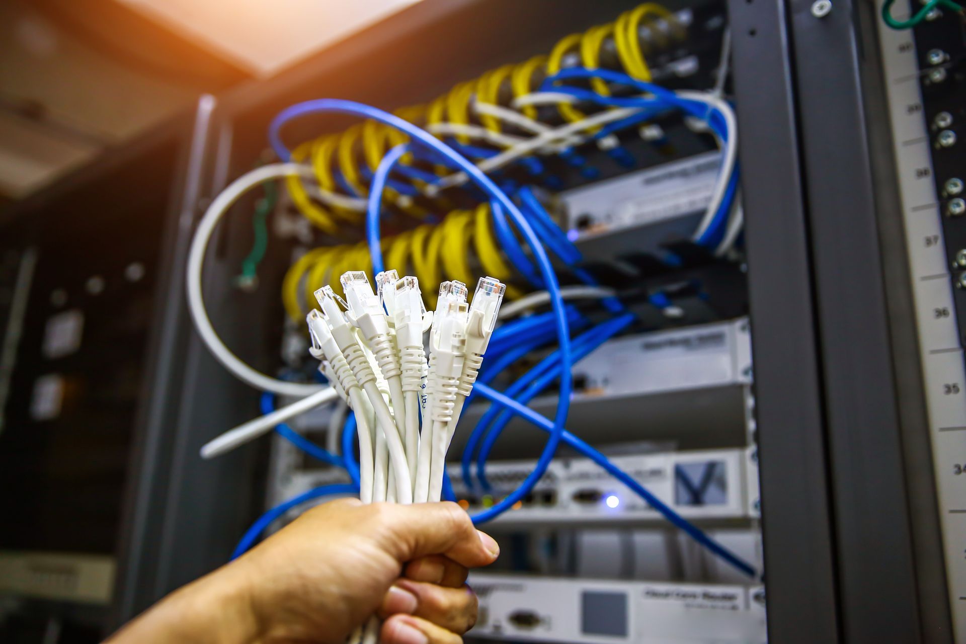 Hand holding bundled white network cables in a server rack with blue Ethernet cords.