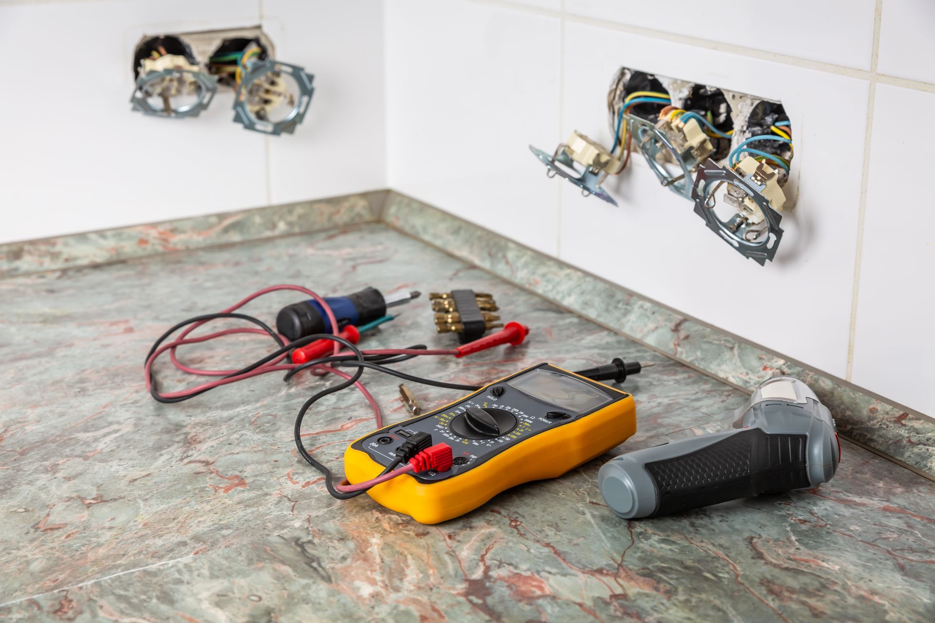 Tools and exposed electrical boxes on a kitchen counter and wall holes