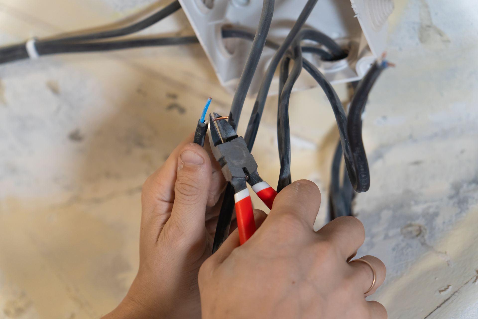 Hands using red wire cutters to trim cables against a wall.