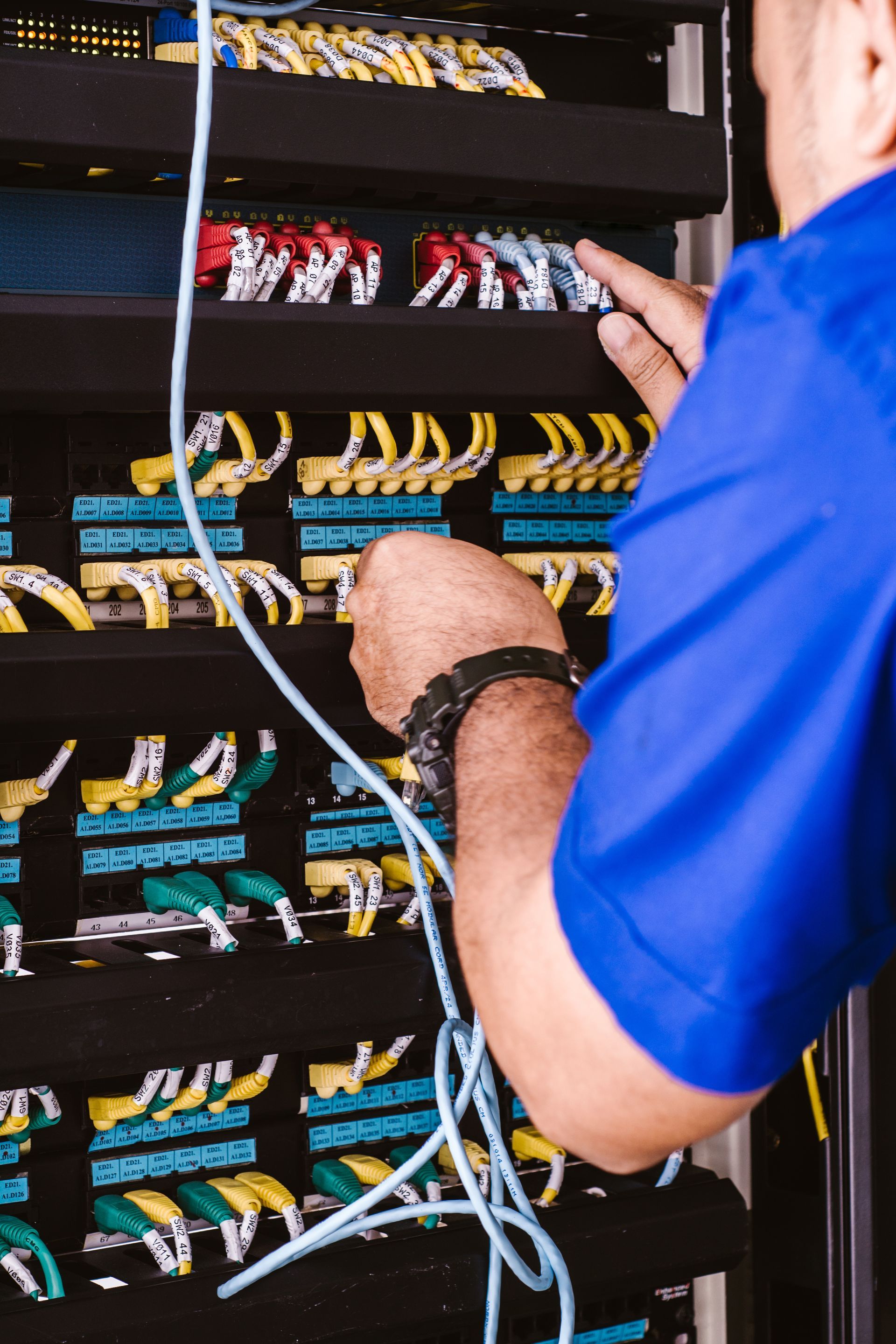 Technician wiring a network switch cabinet with blue and yellow cables