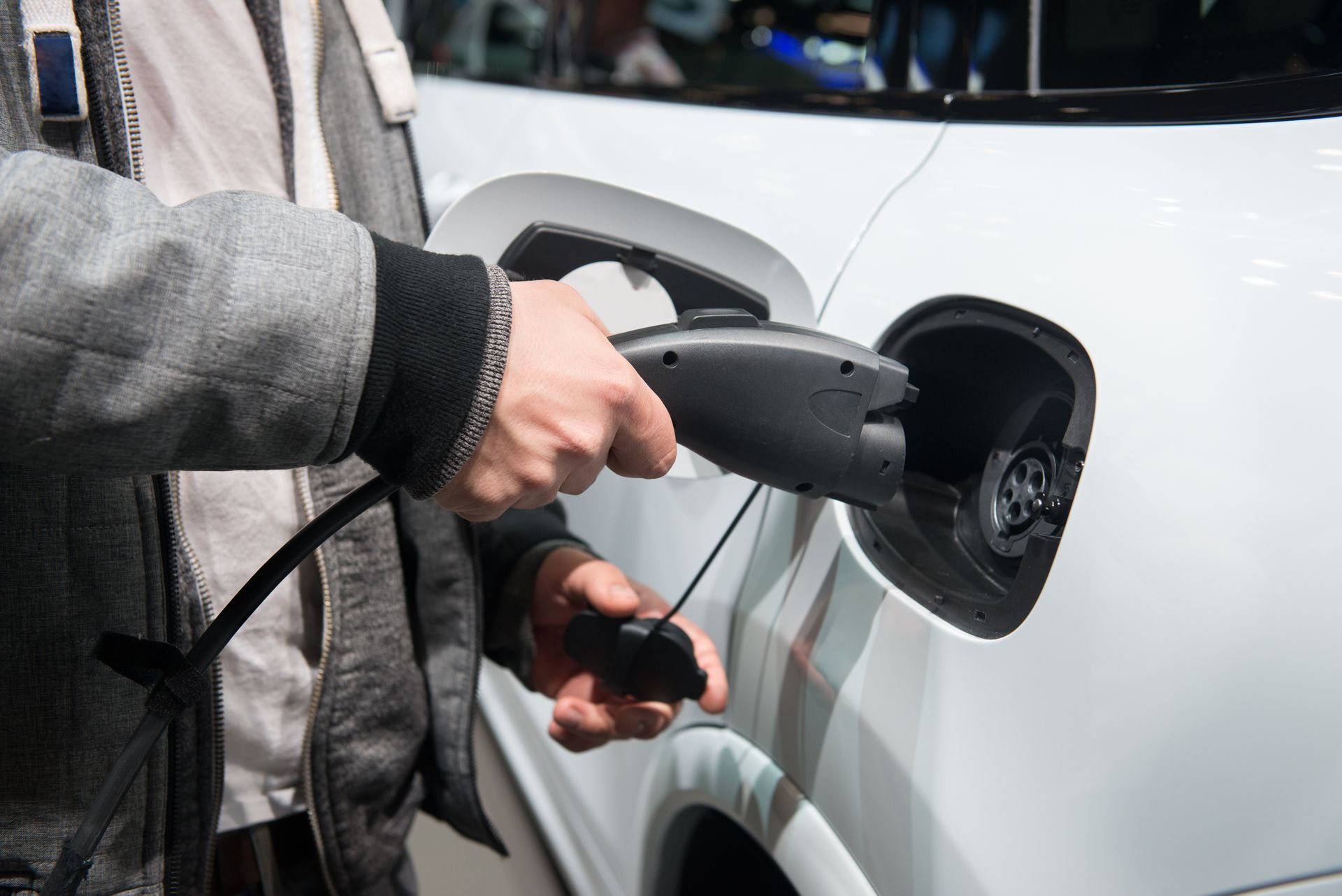 Person charging a white electric car at a public charging station