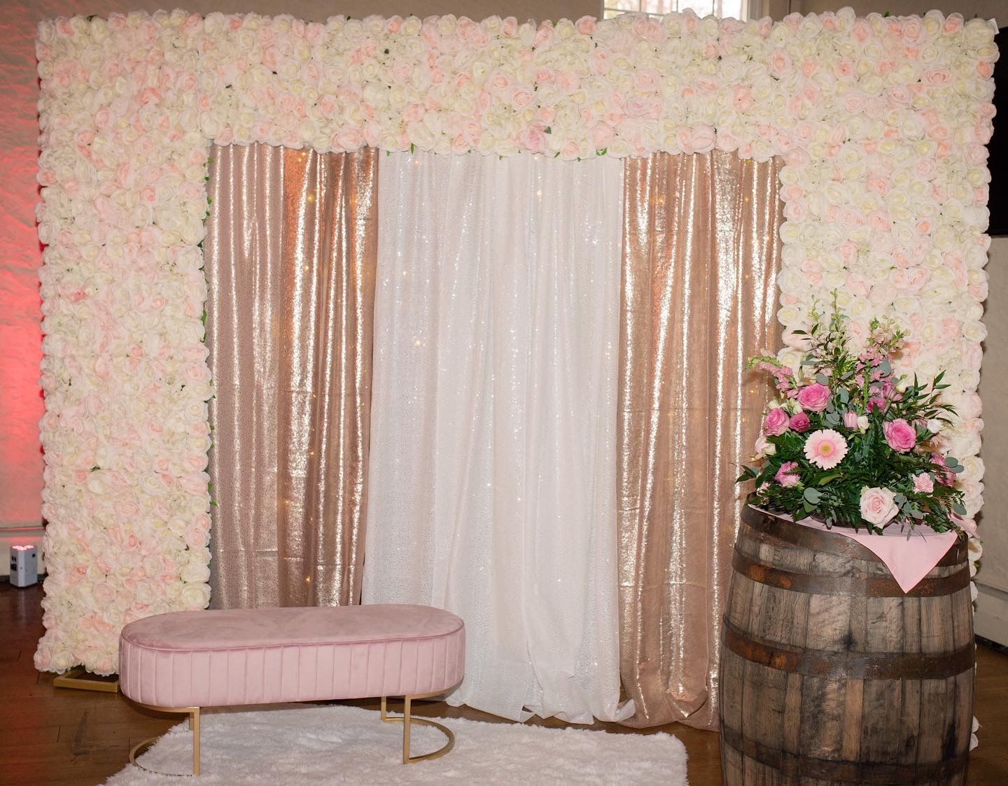 A pink bench is sitting in front of a wall of flowers.