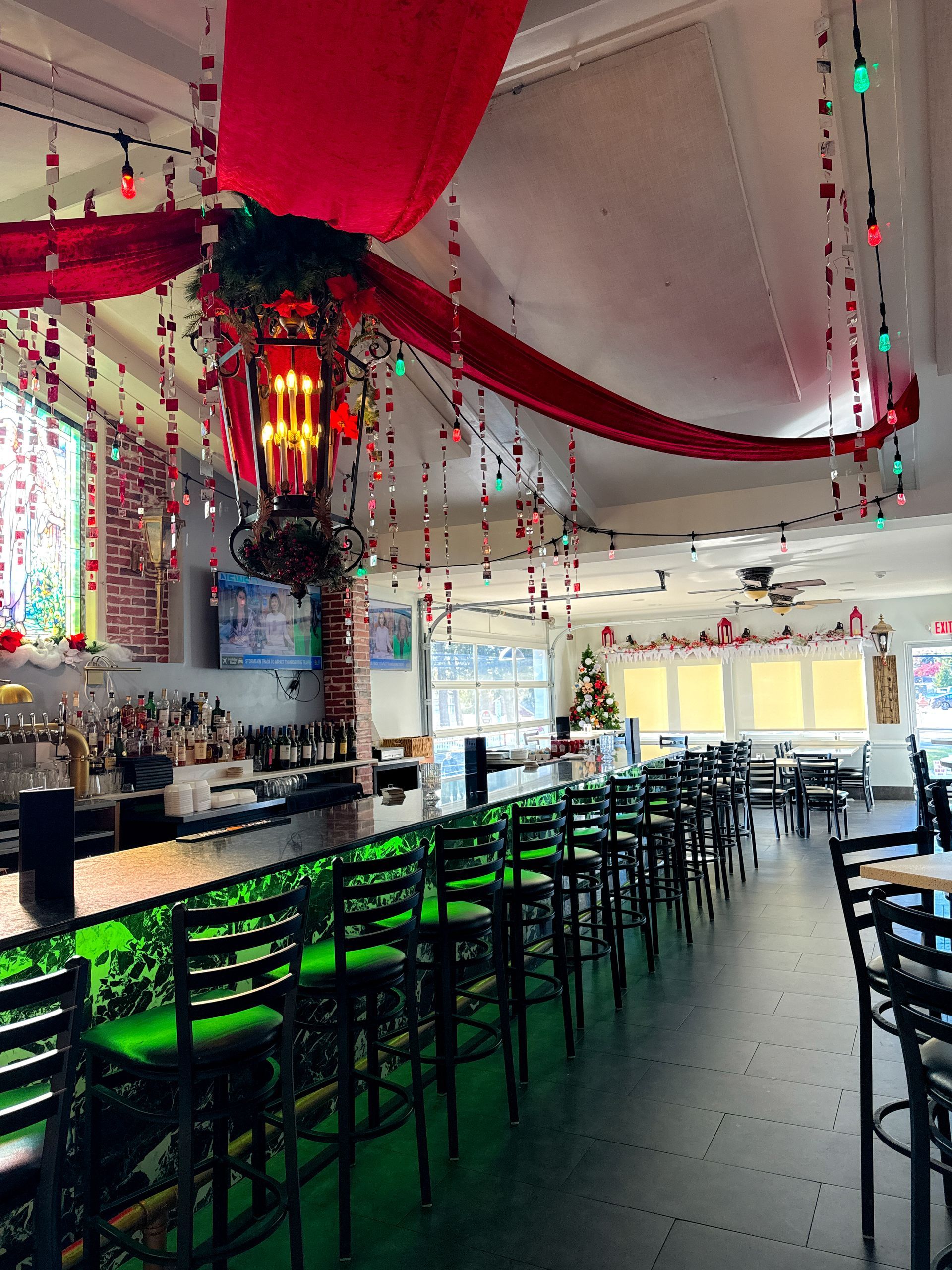 A restaurant with a long bar and tables and chairs decorated for christmas.
