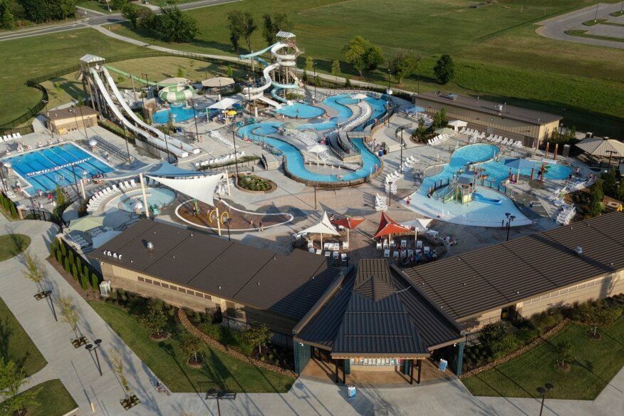 Aerial view of a large outdoor water park with blue pools, winding slides, and a central brown-roofed building