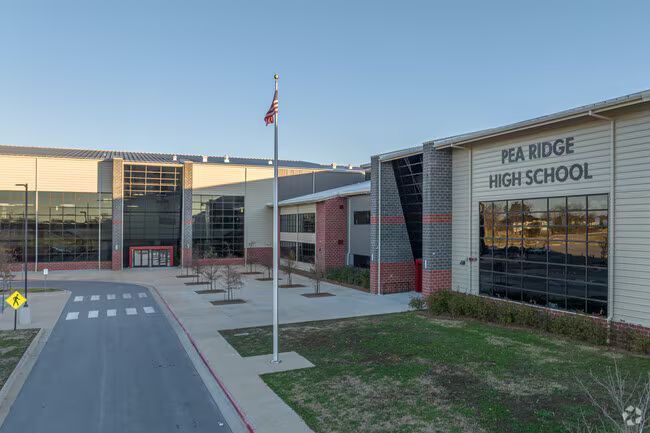 Front entrance of Pea Ridge High School with glass facade, walkway, and flagpole